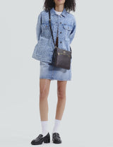 Model wearing a light blue denim jacket and skirt, paired with black loafers, white socks, and carrying a small black Coach crossbody bag